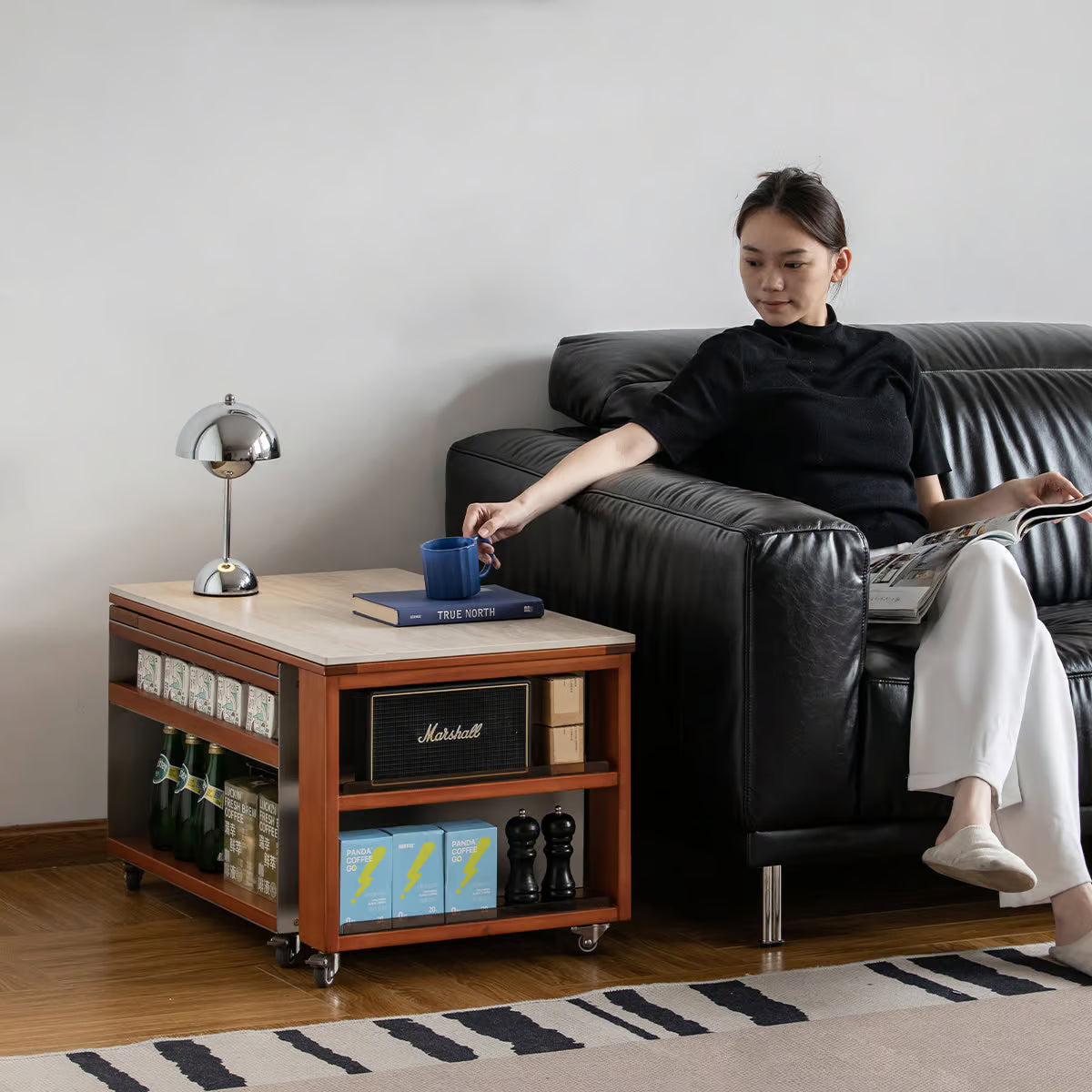 Rolling side table with a stone top beside a sofa holding a mug and a book