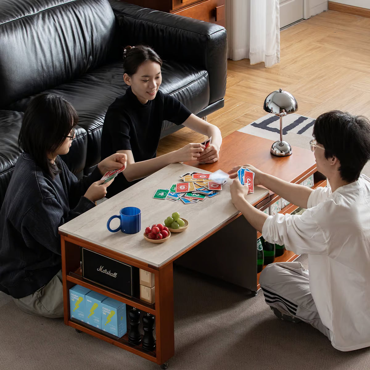 Three people sitting on the floor around a stone top coffee table